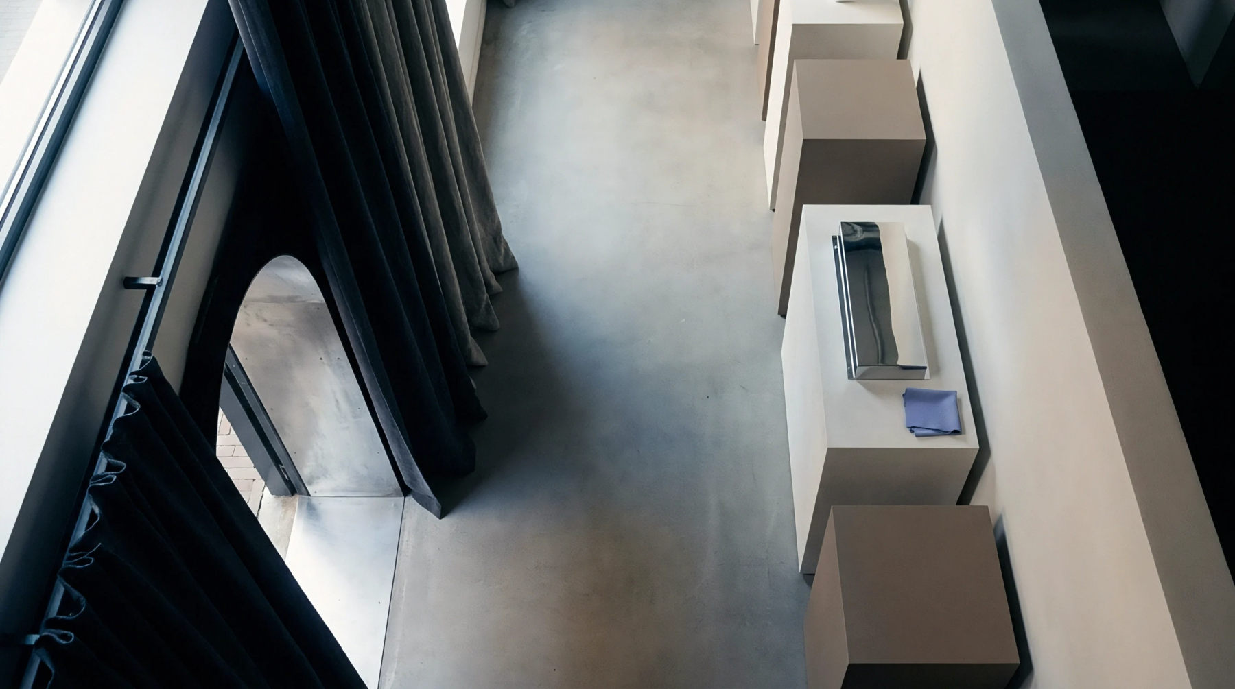 Concrete retail corridor flooring features sequential display blocks and a metal merchandising tray alongside vertical fabric drapery.